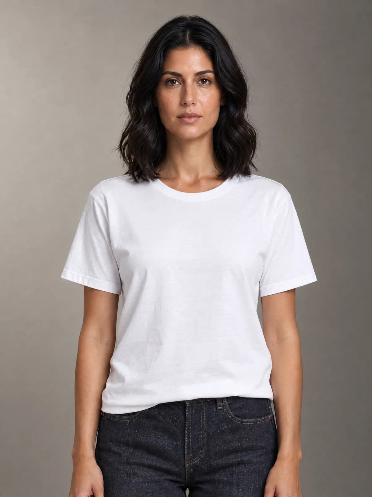 Marta in the white T-shirt and dark jeans, against a warm grey studio backdrop