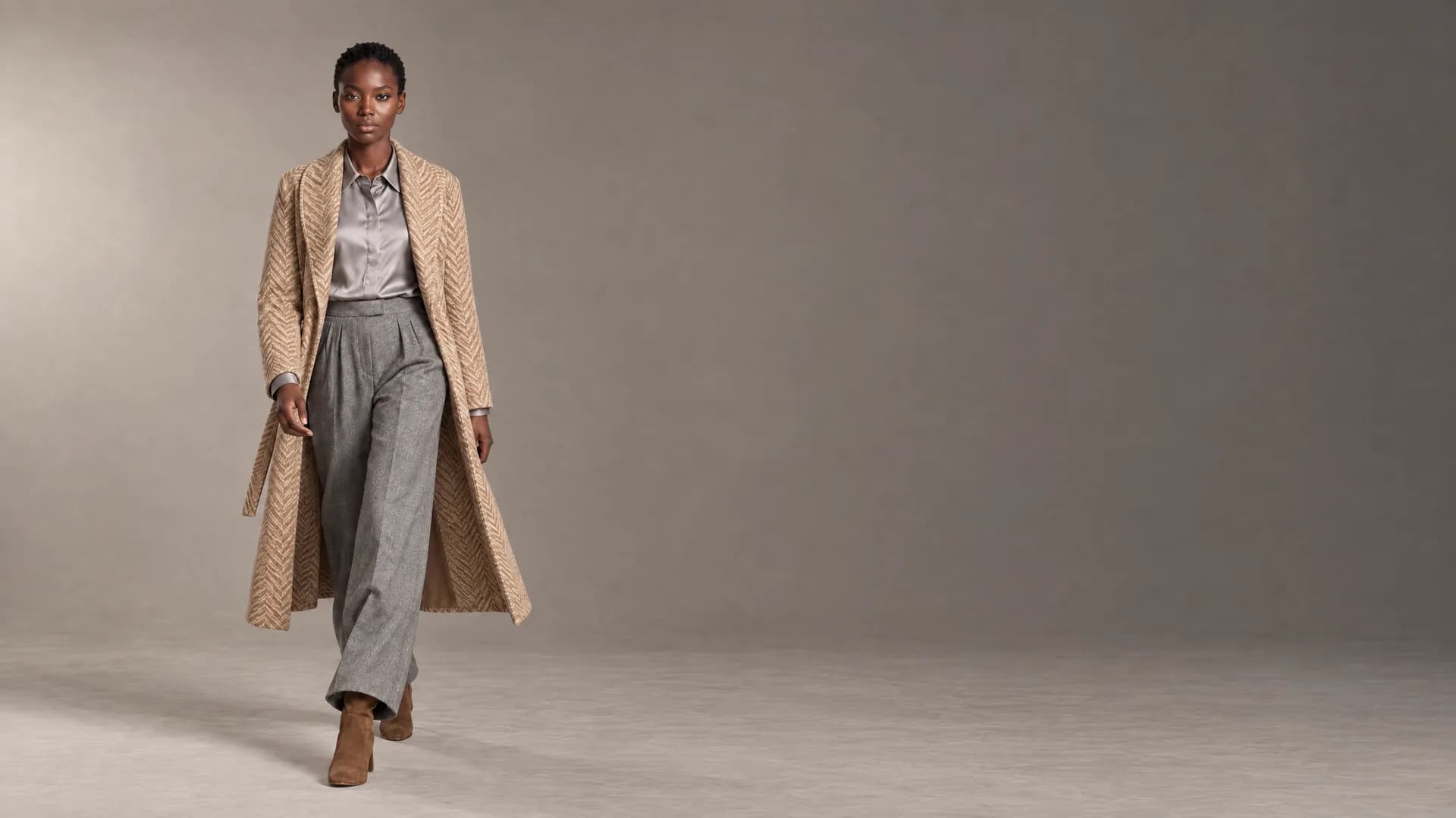 Look 01 in 16:9: Zola on the left in the herringbone coat, the empty warm grey studio on the right